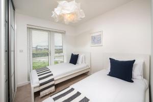 two beds in a room with a window and a chandelier at Footsteps to the beach, Seaviews & Beautiful Sunsets in Westward Ho