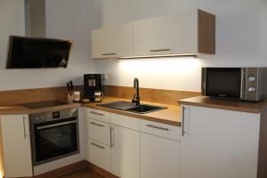 eine Küche mit weißen Schränken, einer Spüle und einer Mikrowelle in der Unterkunft Luxuriöse Stadtwohnungen in Königstein in Königstein an der Elbe