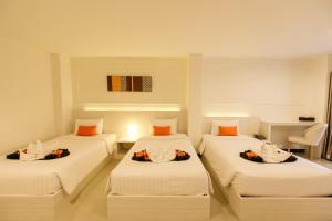 3 camas en una habitación con sábanas blancas y almohadas de color naranja en De Hug Hotel & Residence, en Chiang Rai