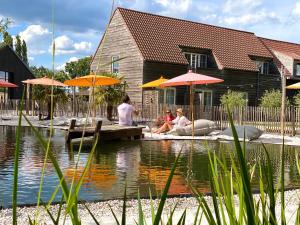 three people sitting on a dock near a pond with umbrellas at Hoeve La Cascina in Deinze