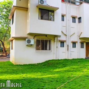 a white house with a window and a green yard at Orchid Anant Holidays in Alibaug