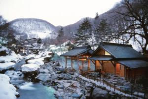 una cabaña de madera en la nieve junto a un río en Takaragawa Onsen Ousenkaku, en Minakami