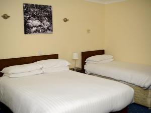 two beds in a hotel room with white sheets at Park Hill Hotel in Lowestoft