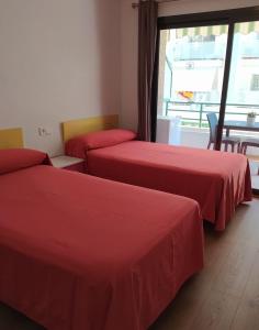 um quarto com duas camas com lençóis vermelhos e uma janela em Hostal Rosa em Villajoyosa