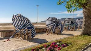 a row of beach chairs with umbrellas on the beach at Apartamento Praia do Relógio in Figueira da Foz