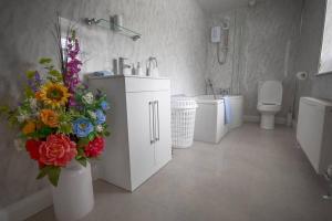 a bathroom with a sink and a toilet and flowers at Neds Brae View in the Glens of Antrim Family and Pet friendly Carnlough home in Carnlough