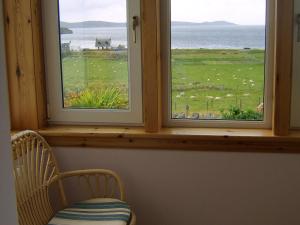 una camera con due finestre con una sedia e una vista su un campo di Top House a Ullapool