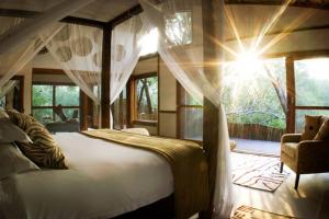 a bedroom with a bed and a chair and windows at Ihlozi Bush Lodge in Hluhluwe