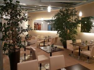 un restaurante con mesas, sillas blancas y plantas en City Hotel Stuttgart, en Stuttgart