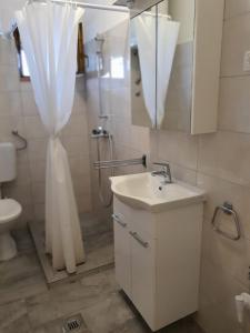 a bathroom with a sink and a shower with a shower curtain at Guesthouse Mila in Tisno