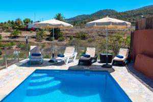 a swimming pool with chairs and umbrellas in front of a house at Casa la Viña in Puntagorda