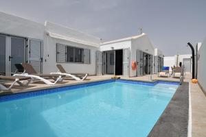 a swimming pool with chairs and a house at Villa Malagueñas in Puerto del Carmen