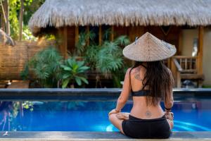 a woman in a hat sitting next to a swimming pool at H2O Peaceful Yoga Resort in Gili Islands