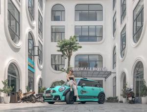 a woman sitting on the hood of a car in front of a building at MOMALI Hotel Ninh Binh in Ninh Binh