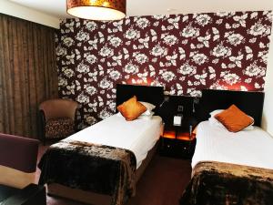 2 camas en una habitación de hotel con papel pintado floral en The BlueBell Hotel en Neath