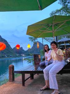two women sitting on a bench under an umbrella at Son Doong Riverside in Phong Nha