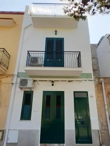 a white building with green doors and a balcony at La Casetta sul Mare in Isola delle Femmine