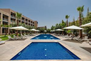 ein Pool in einem Hotel mit Stühlen und Sonnenschirmen in der Unterkunft Wazo Hotel in Marrakesch