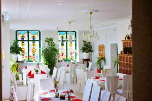 Ratskeller Hotel & Restaurant Lindow في ليندو: غرفة بها طاولات وكراسي بيضاء ونوافذ زجاجية ملطخة