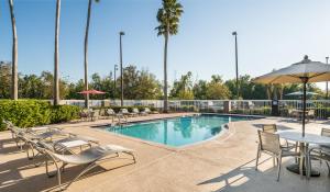 uma piscina com cadeiras e mesas e um guarda-sol em Holiday Inn Express & Suites Orlando International Airport, an IHG Hotel em Orlando