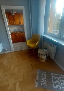 a living room with a yellow chair and a kitchen at Apartament Pod Lasem in Gdańsk