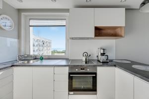 kuchnia z białymi szafkami, zlewem i oknem w obiekcie Comfort Apartments Wyspiańskiego w mieście Gdynia