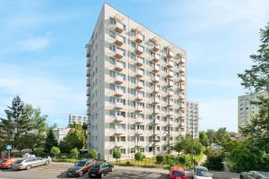 wysoki biały budynek z samochodami zaparkowanymi na parkingu w obiekcie Comfort Apartments Wyspiańskiego w mieście Gdynia