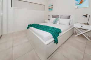 a white bedroom with a bed with a green blanket on it at Apartment Close to the City Life on Lake 3 in Cairns North
