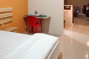 1 dormitorio con 1 cama y escritorio con silla roja en RedDoorz Syariah @ Haurgeulis, en Baoen