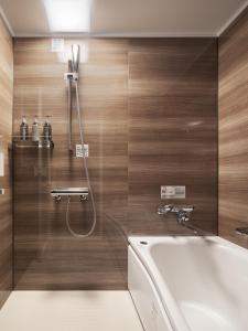 a bathroom with a tub and a shower with wooden walls at Nest Hotel Hiroshima Ekimae in Hiroshima