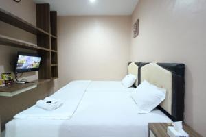 um quarto com uma cama com lençóis brancos e uma televisão em O2 Residence em Medan
