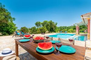 a wooden table with watermelon plates and wine glasses next to a pool at Beach Villa Joanna by PosarelliVillas in Acharavi