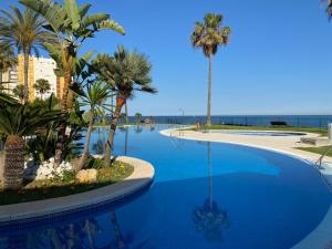 a large blue swimming pool with palm trees and the ocean at Mi Capricho Apartment with Sea Views and Gardens in La Cala de Mijas