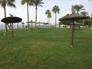 a group of straw umbrellas in a field with palm trees at Mi Capricho Apartment with Sea Views and Gardens in La Cala de Mijas