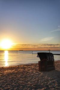 a bench on a beach with the sunset in the background at Backbord in Wangerland +2 photos