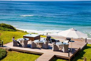 une terrasse avec des tables, un parasol et l'océan dans l'établissement African Oceans Manor on the Beach, à Mossel Bay