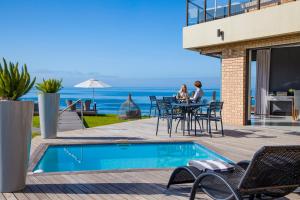 two women sitting at a table by a swimming pool at African Oceans Manor on the Beach in Mossel Bay