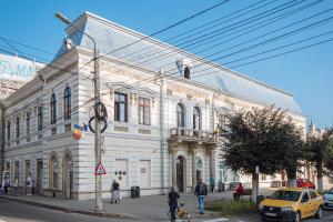 a large white building on a street with a yellow taxi at Buchenland Hotel in Câmpulung Moldovenesc