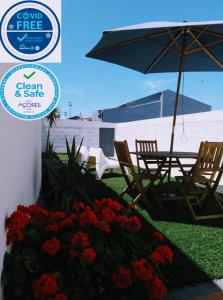 eine Terrasse mit Stühlen, einem Sonnenschirm und Blumen in der Unterkunft Casa do Califórnia in Ribeira Grande