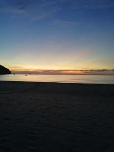 a beach with the sun setting over the water at Rainbow Tioman Cottage in Kampong Juara