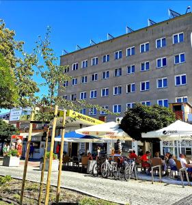 personas sentadas en mesas bajo sombrillas frente a un edificio en Posejdon, en Międzyzdroje