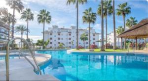 a large swimming pool with palm trees and a building at Mi Capricho in Sitio de Calahonda