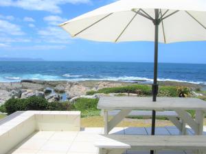 Beachfront House - Hermanus Whale View في هيرمانوس: طاولة نزهة بيضاء مع مظلة والمحيط