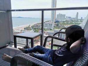 Un niño pequeño sentado en una silla en un balcón en Kuno - 2Br, Beachfront Jomtien en Jomtien Beach