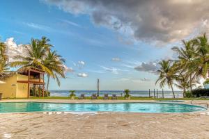 a swimming pool with palm trees and the ocean at Marechiaro - Apartamento Vista Al Mar - Playa Juan Dolio in Juan Dolio