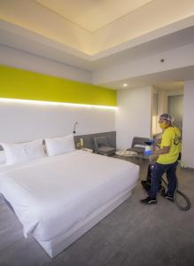 a man vacuum cleaning a hotel room with a large bed at YELLO Hotel Paskal Bandung in Bandung