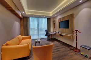 a hotel room with a couch and a desk and a television at The Fern Royal Farm Resort, Anjar in Anjār