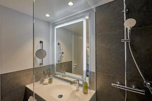 a bathroom with a sink, mirror, and bath tub at H4 Hotel Leipzig in Leipzig