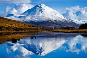 een besneeuwde berg met een reflectie in een meer bij Donegal Wild Atlantic Hostel in Dungloe