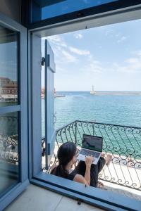 eine Frau auf einem Balkon mit einem Laptop in der Unterkunft Elia Zampeliou Hotel in Chania